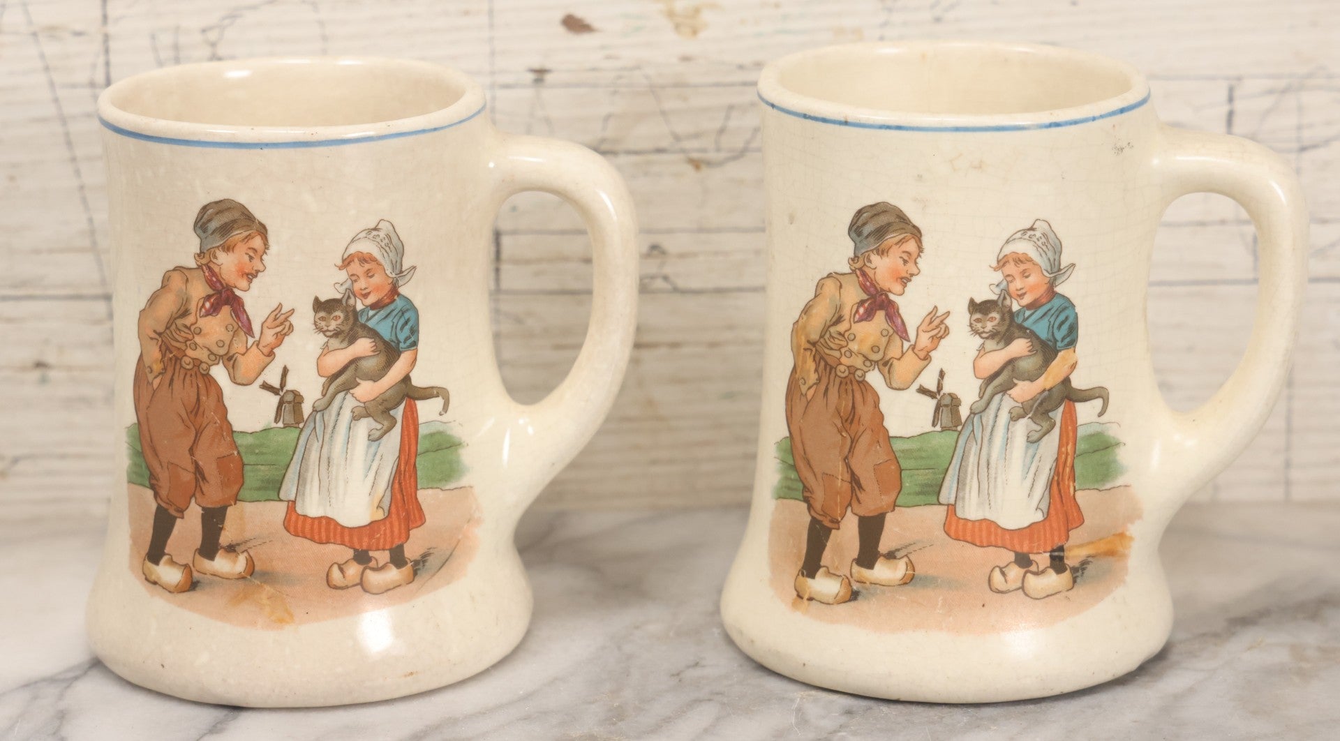 Lot 040 - Pair Of Antique Mugs With Image Of Dutch Children In Clogs Playing With Their Kitten, Windmill In Background