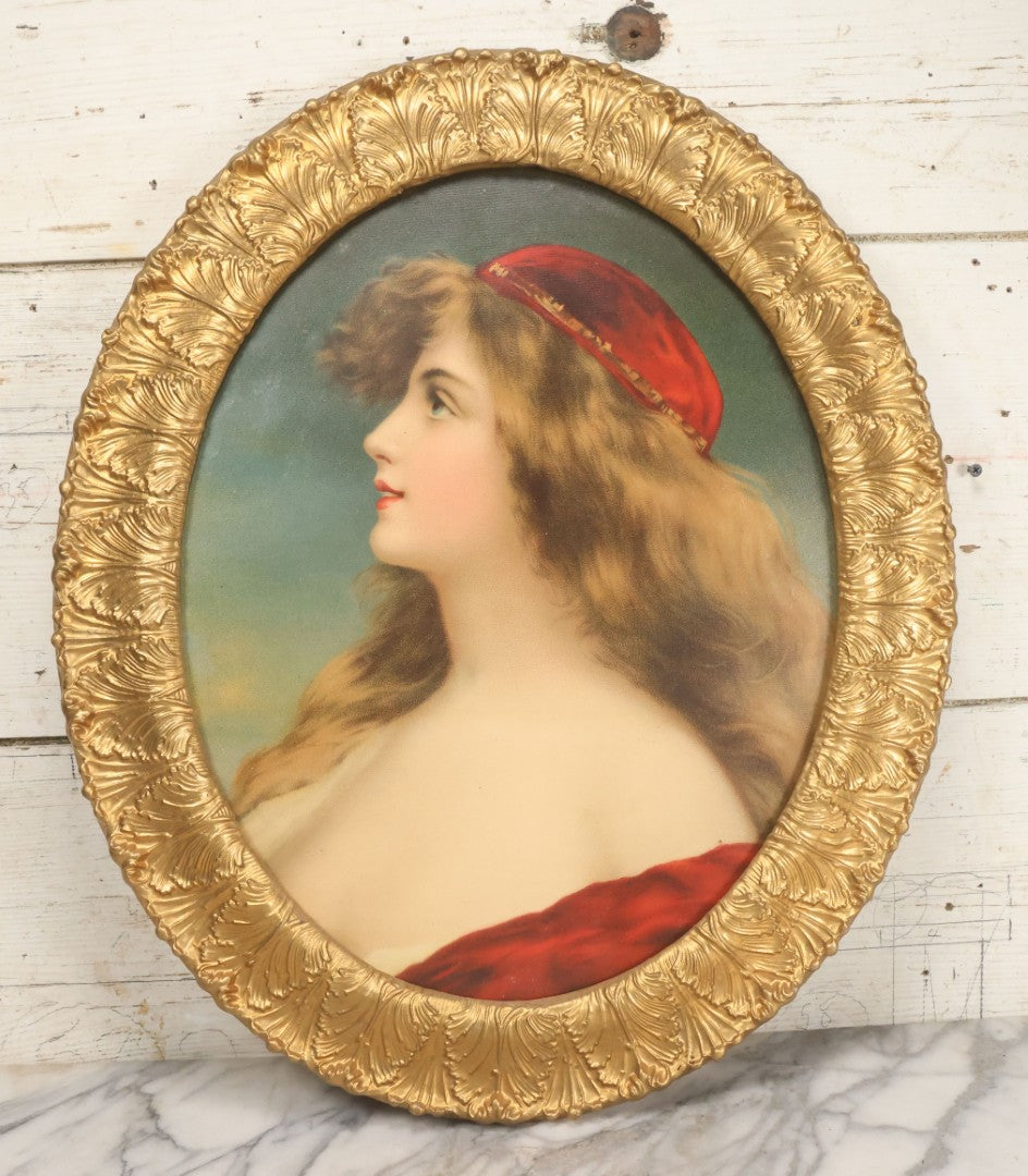 Lot 006 - Antique Chromolithograph Portrait Print Of Blue-Eyed Brunette Beauty With Red Velvet Cap And Loose Fitting Red Gown In Ornate Gilded Molded Gesso Oval Frame, 21" x 25"