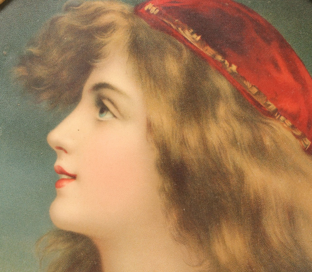 Lot 006 - Antique Chromolithograph Portrait Print Of Blue-Eyed Brunette Beauty With Red Velvet Cap And Loose Fitting Red Gown In Ornate Gilded Molded Gesso Oval Frame, 21" x 25"