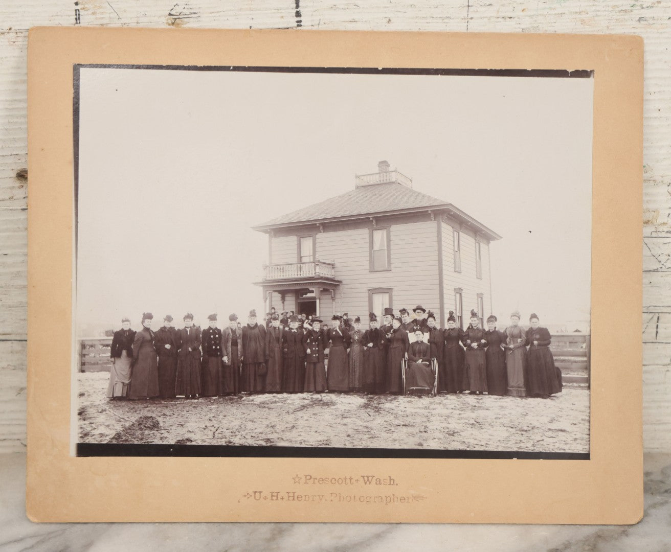 Lot 140 - Antique Boarded Photograph Of Group Of Women In Dark Attire Posing Outside Two Story Home, Including Men In Top Hats And Woman In Wheelchair, Photographed By U.H. Henry, Prescott, Washington