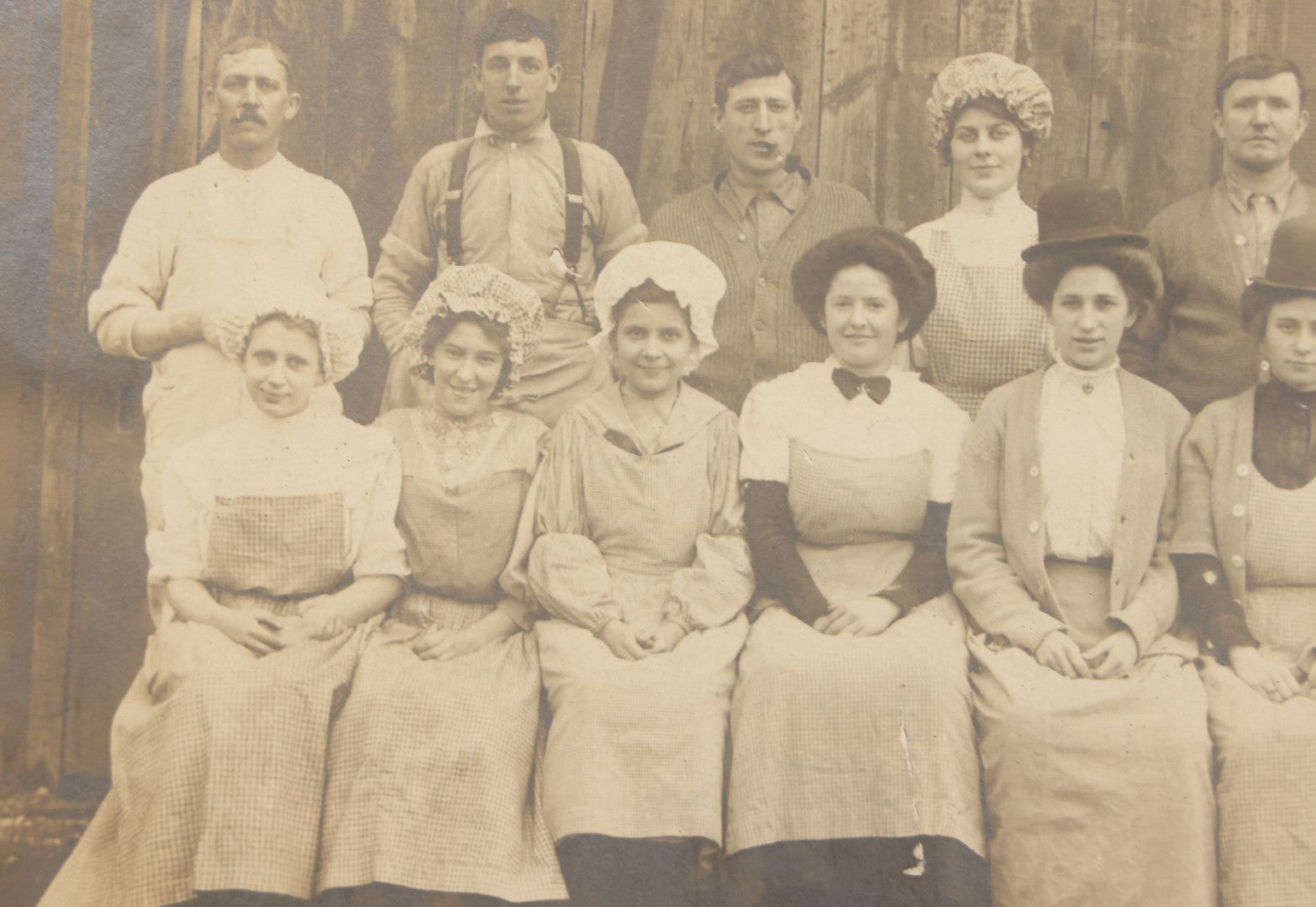 Lot 142 - Antique Boarded Occupational Photograph Of Men And Women Workers Posing In Workwear Outside A Barn, Women In Bowler Hats And Bonnets And Man Smoking Pipe