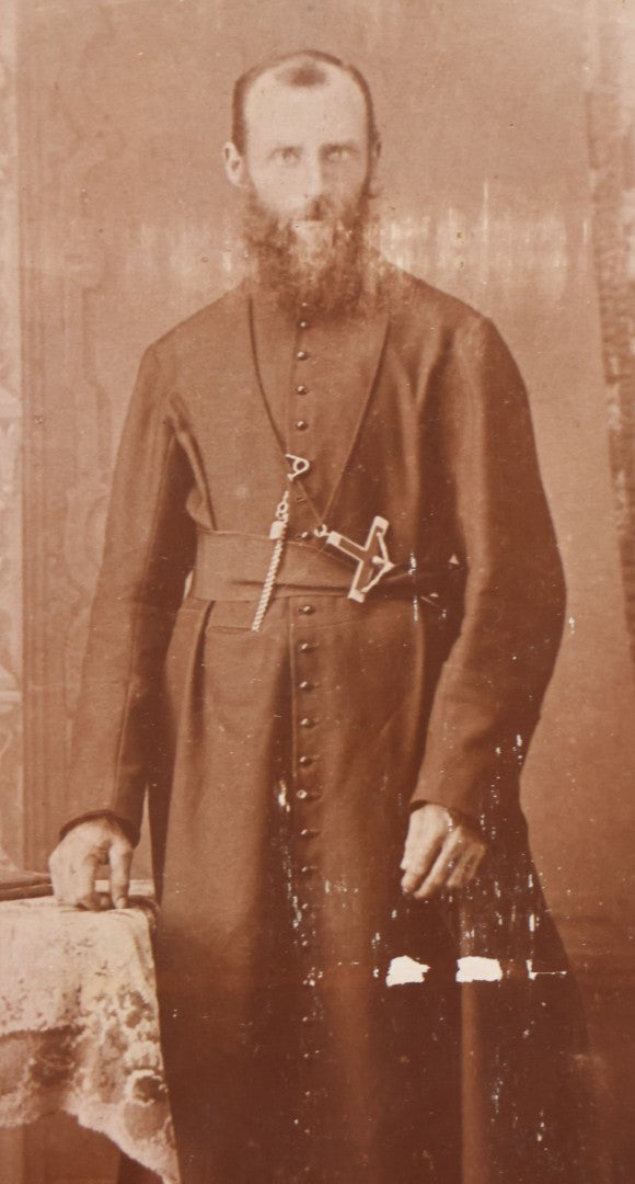 Lot 019 - Antique Cabinet Card Photograph Of A Bearded Priest In Black Robe With Large Pectoral Crucifix Tucked In Belt, Frank Lariviere, Photographer, Central Falls & Pawtucket, Rhode Island