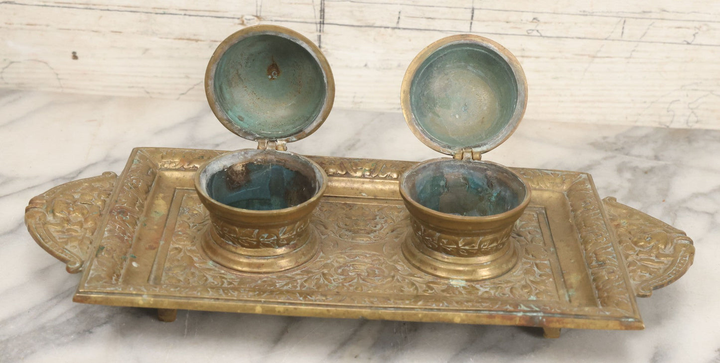Lot 027 - Antique Cast Brass Double Inkwell And Desk Tray With Cherub And Green Man Motifs, Hinged Lids, Underside Marked 3143, No Inserts