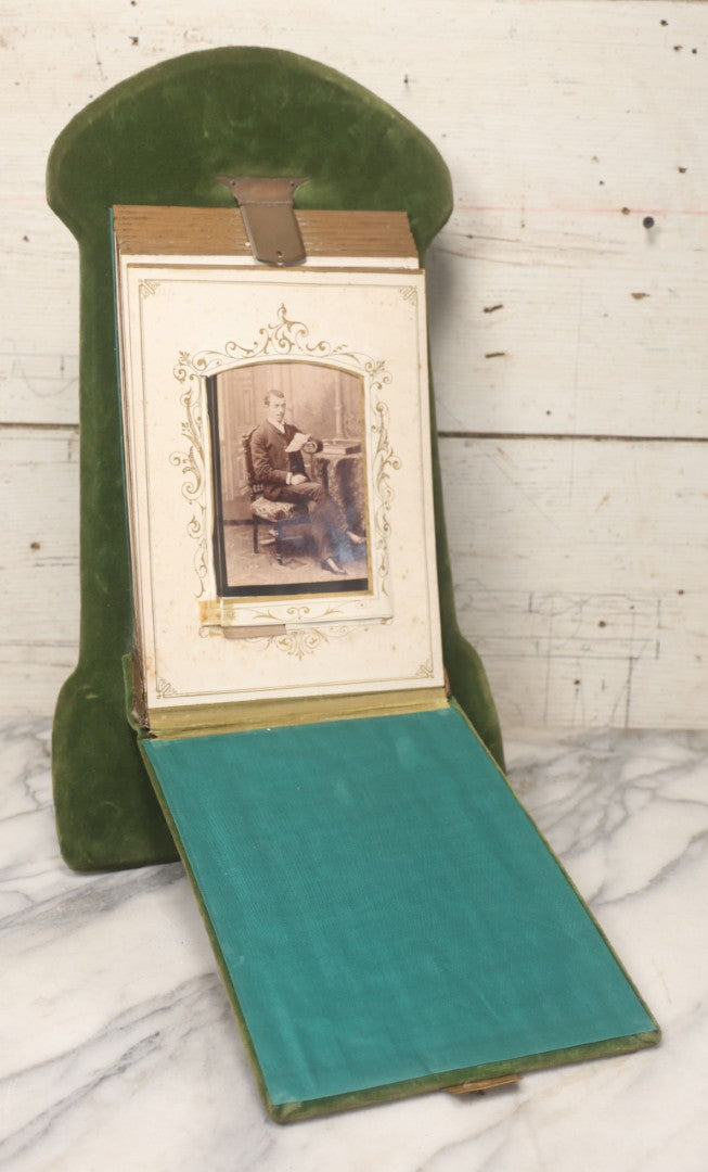 Lot 010 - Antique Victorian Green Velvet Display Photo Album With Stand And Tilt Down Cover, Brass Adornments, Containing 12 Cabinet Card And 24 C.D.V. Photographs And Images, Including Man Posing With Rifle, Sailor In Uniform, And Men Smoking