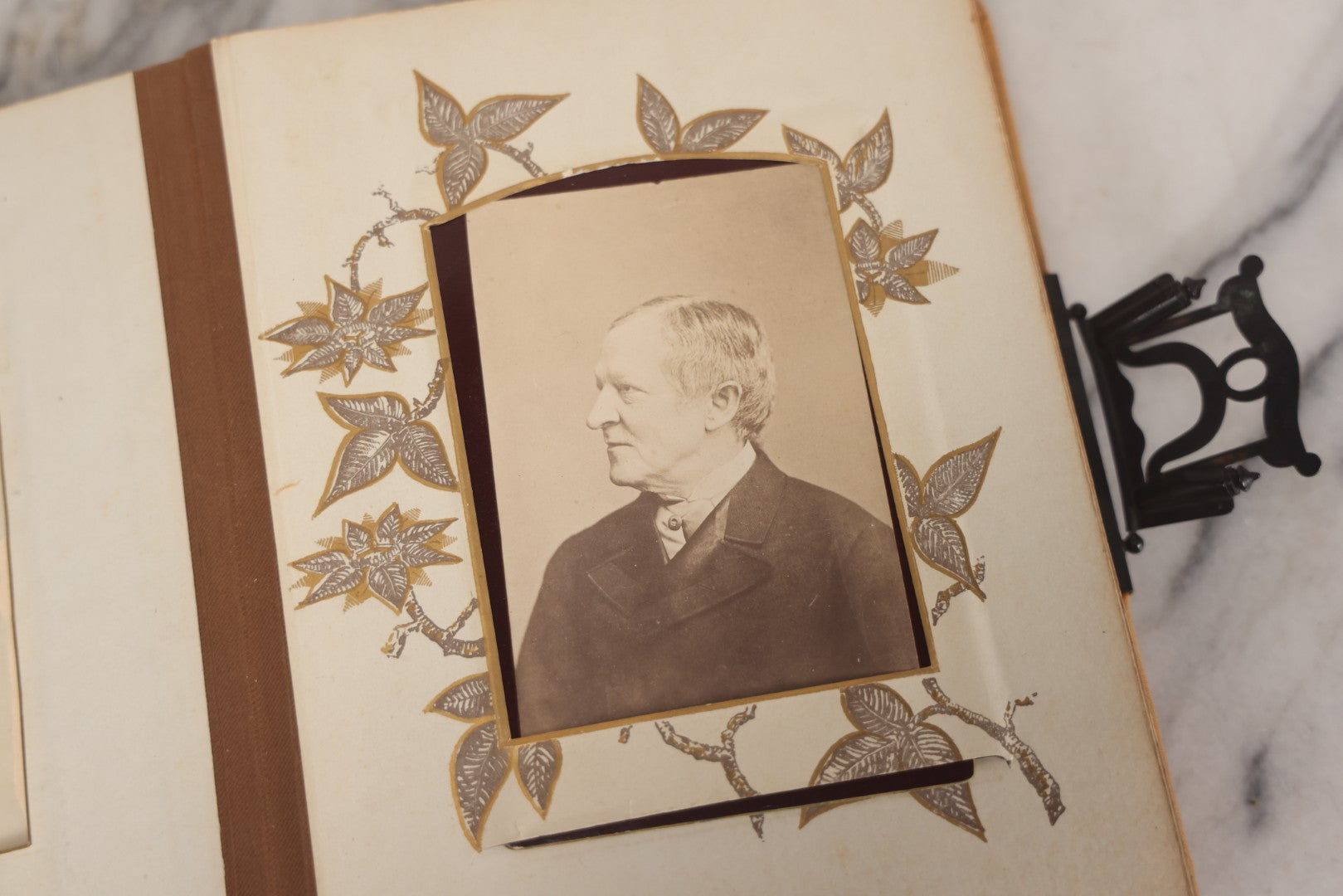 Lot 012 - Antique Victorian Photo Album With Wood Cover And Silverplate Emblem, Containing Twenty Antique Photographs Of Various Types, Including Man In Office, Children With Pram, Man With White Beard, Note Binding Wear Cover Loosening