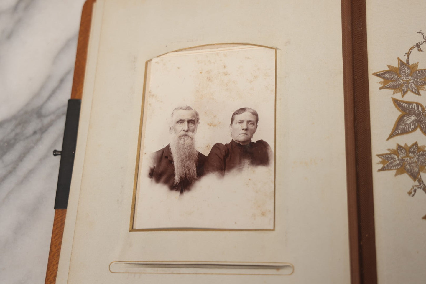 Lot 012 - Antique Victorian Photo Album With Wood Cover And Silverplate Emblem, Containing Twenty Antique Photographs Of Various Types, Including Man In Office, Children With Pram, Man With White Beard, Note Binding Wear Cover Loosening
