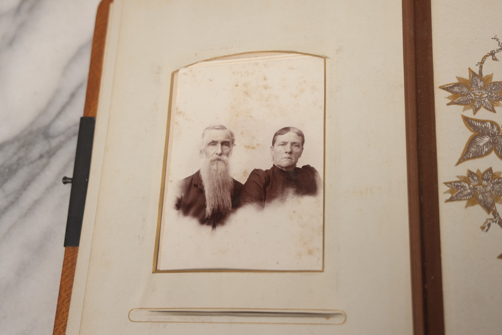 Lot 012 - Antique Victorian Photo Album With Wood Cover And Silverplate Emblem, Containing Twenty Antique Photographs Of Various Types, Including Man In Office, Children With Pram, Man With White Beard, Note Binding Wear Cover Loosening