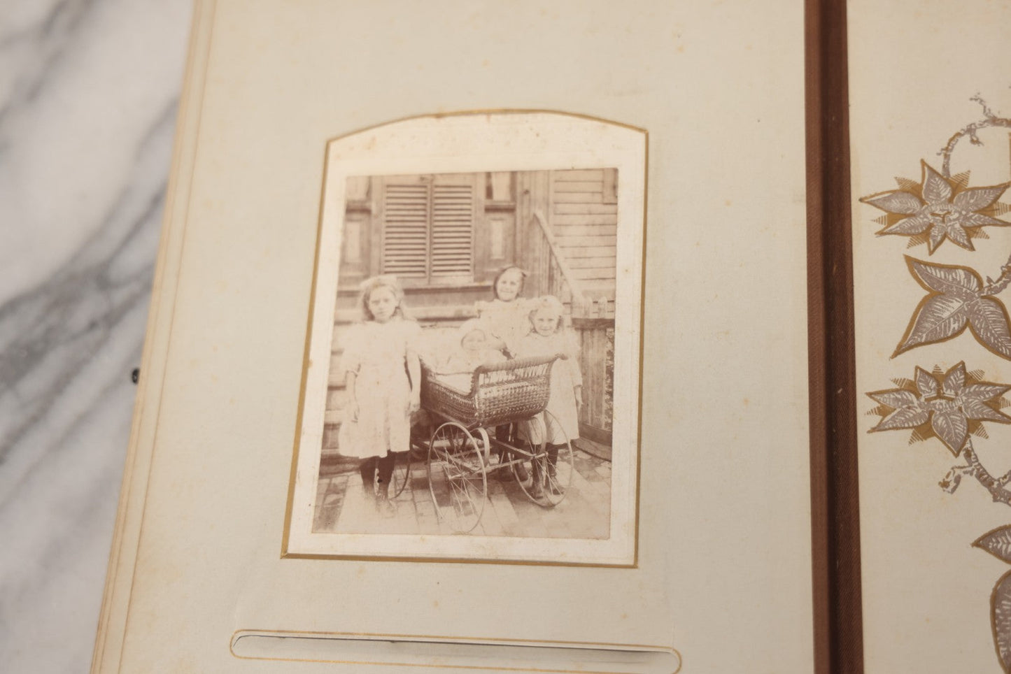 Lot 012 - Antique Victorian Photo Album With Wood Cover And Silverplate Emblem, Containing Twenty Antique Photographs Of Various Types, Including Man In Office, Children With Pram, Man With White Beard, Note Binding Wear Cover Loosening