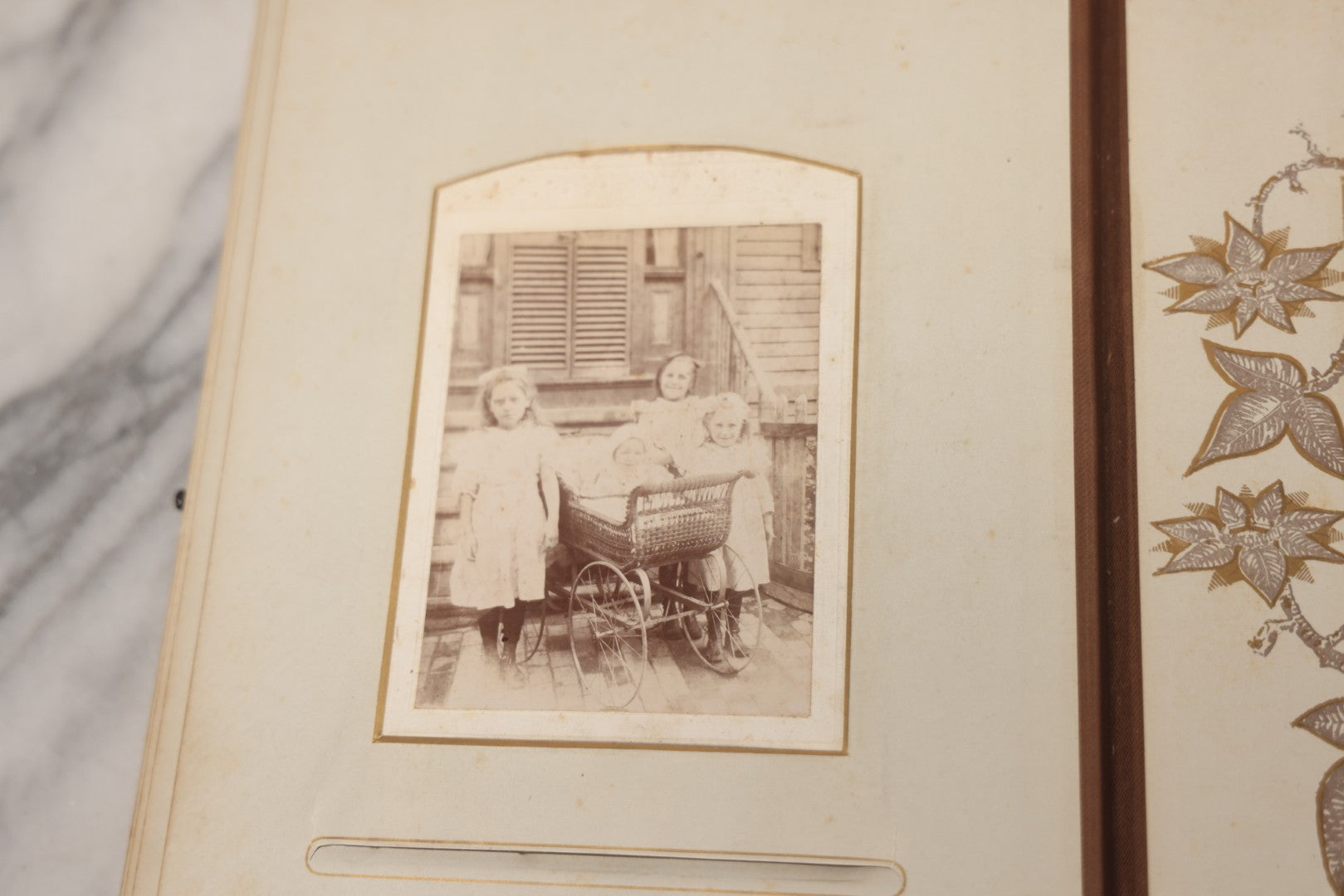 Lot 012 - Antique Victorian Photo Album With Wood Cover And Silverplate Emblem, Containing Twenty Antique Photographs Of Various Types, Including Man In Office, Children With Pram, Man With White Beard, Note Binding Wear Cover Loosening