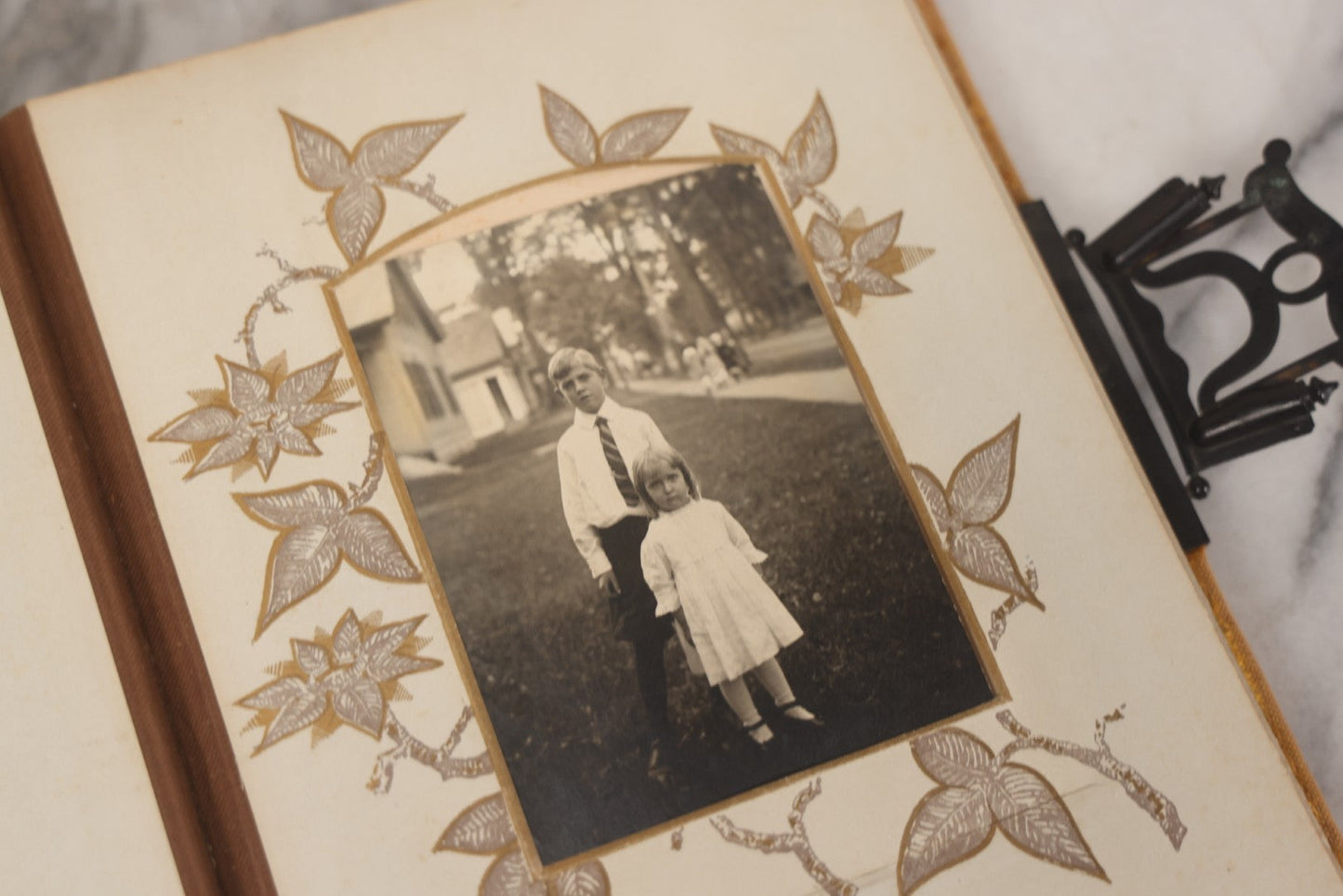 Lot 012 - Antique Victorian Photo Album With Wood Cover And Silverplate Emblem, Containing Twenty Antique Photographs Of Various Types, Including Man In Office, Children With Pram, Man With White Beard, Note Binding Wear Cover Loosening
