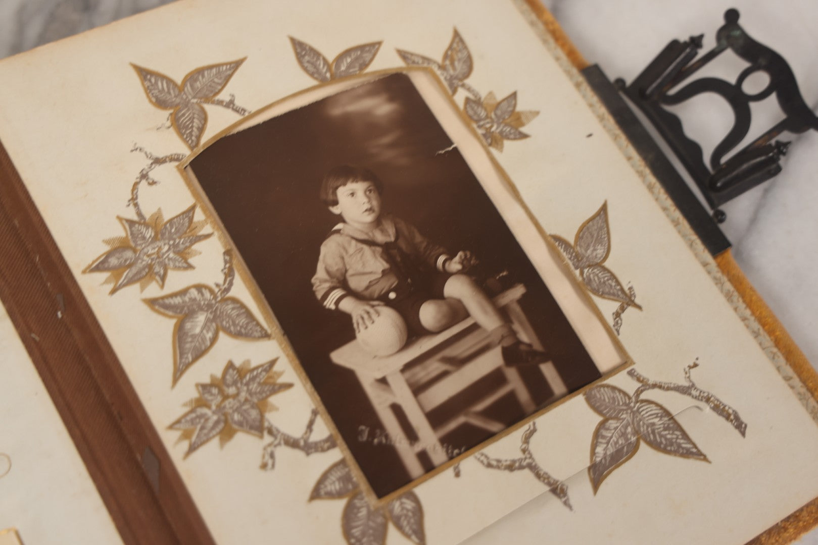 Lot 012 - Antique Victorian Photo Album With Wood Cover And Silverplate Emblem, Containing Twenty Antique Photographs Of Various Types, Including Man In Office, Children With Pram, Man With White Beard, Note Binding Wear Cover Loosening