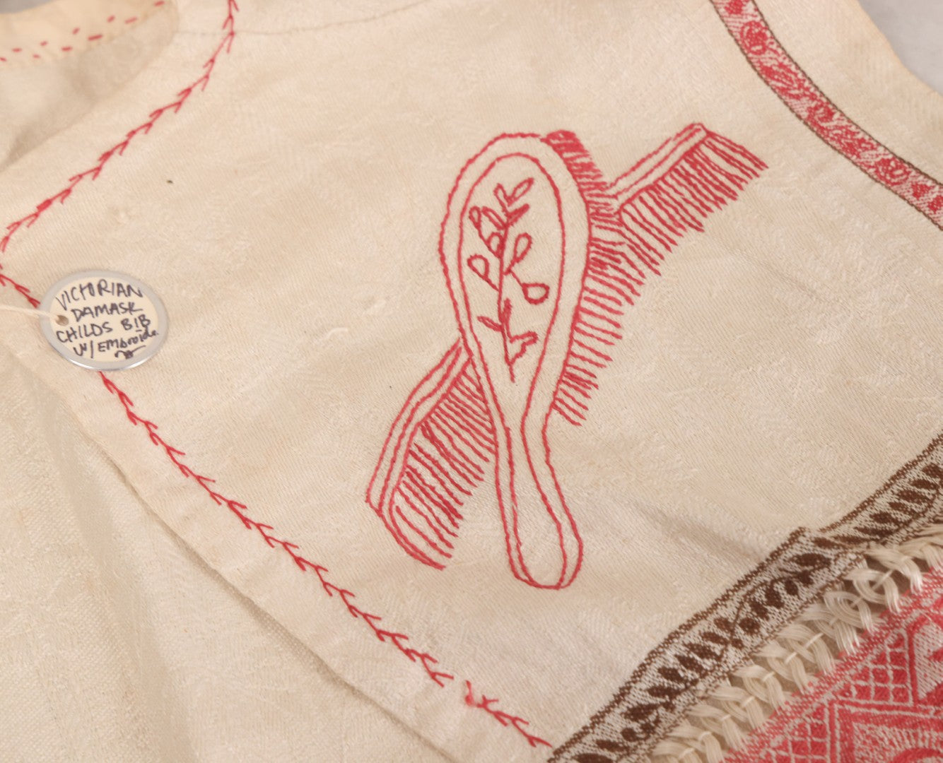Lot 035 - Antique Damask Textile Fabric Bib With Detailed Red Embroidery Featuring All Seeing Eye, Comb And Brush And Hairpin Motifs