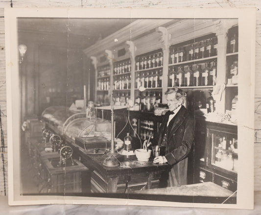 Lot 093 - Antique Large Format Photograph Of Elderly Pharmacist Compounding Medicine At The Pharmacy Counter, With Many Apothecary Bottles And Tools Visible