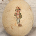 Lot 017 - Antique Genuine Ostrich Egg Specimen With Two Applied Victorian Die Cut Scraps Of Cheeky Caricatures, Note Originally Had More Scraps Attached, As Found