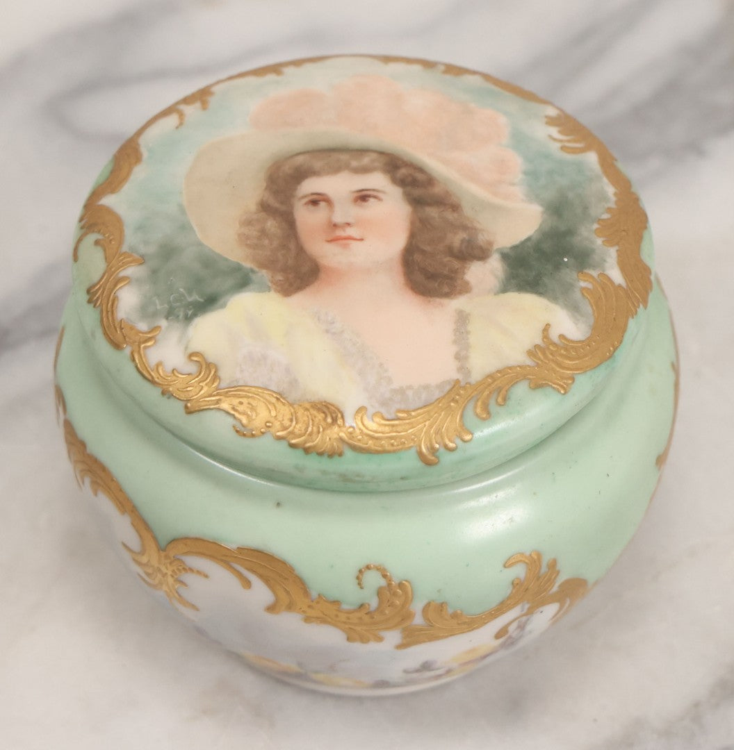 Lot 019 - Antique Hand Painted French Limoges Porcelain Dresser Box With Painting Of Brunette Woman In Extravagant Hat On Lid, With Yellow Painted Flowers, Artist Signed L.C.K. Dated 1894, With Purple "Belleek" Hallmark