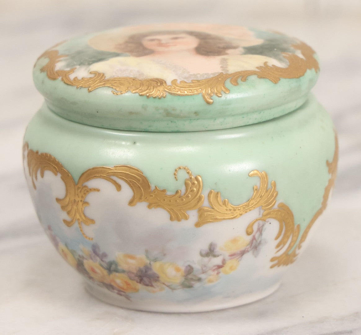Lot 019 - Antique Hand Painted French Limoges Porcelain Dresser Box With Painting Of Brunette Woman In Extravagant Hat On Lid, With Yellow Painted Flowers, Artist Signed L.C.K. Dated 1894, With Purple "Belleek" Hallmark