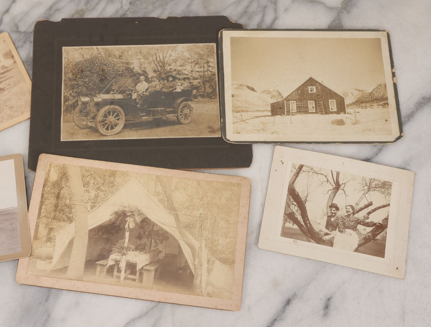 Lot 078 - Grouping Of Six Antique Boarded Outdoor Photographs Including Group In Car, Tent Decorated For Dinner Party, Couple Laughing In Tree, And Western Cabin