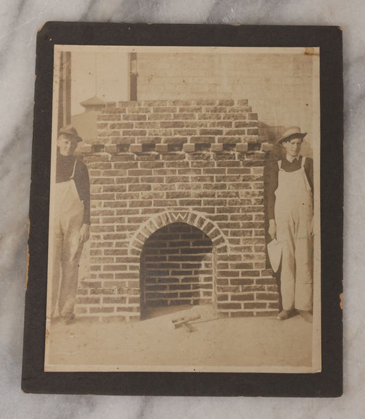 Lot 091 - Antique Boarded Photograph Of Two Young Bricklayers Posing With Tools In Front Of Newly Finished Fireplace With "W" Monogram