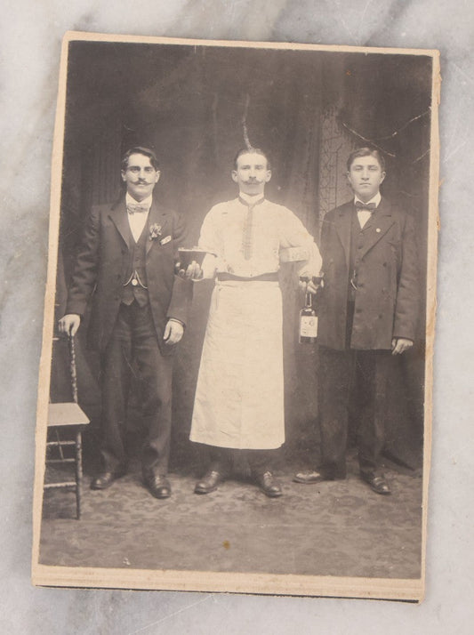 Lot 100 - Antique Trimmed Boarded Photograph Of Bartender Posing With Liquor Bottle, Glasses, And Cigar Box, With Two Men, Detailed Writing On Verso Likely In Polish