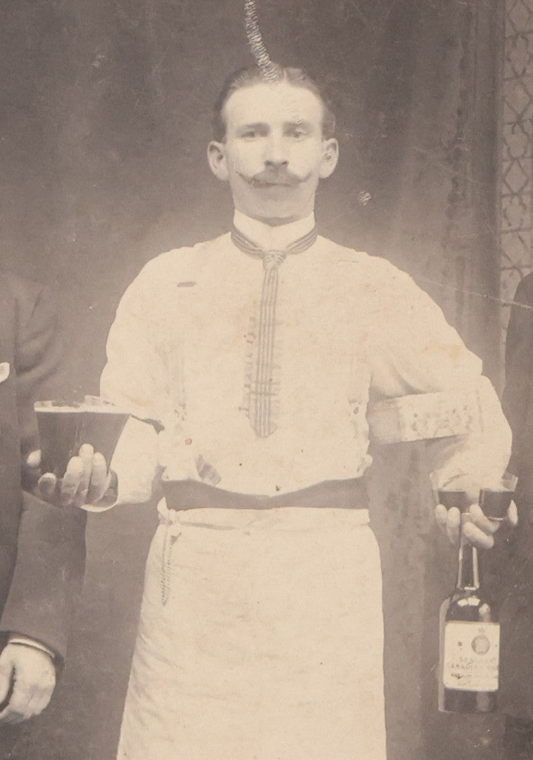Lot 100 - Antique Trimmed Boarded Photograph Of Bartender Posing With Liquor Bottle, Glasses, And Cigar Box, With Two Men, Detailed Writing On Verso Likely In Polish