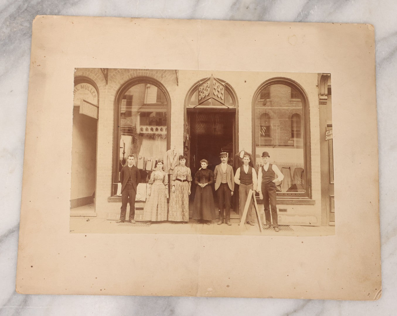 Lot 111 - Antique Boarded Occupational Photograph Of Workers And Dressmakers Posing Outside Their Shop, With Many Signs And Advertisements In Photo, Note Photo Has Large Crease Through Center On Verso