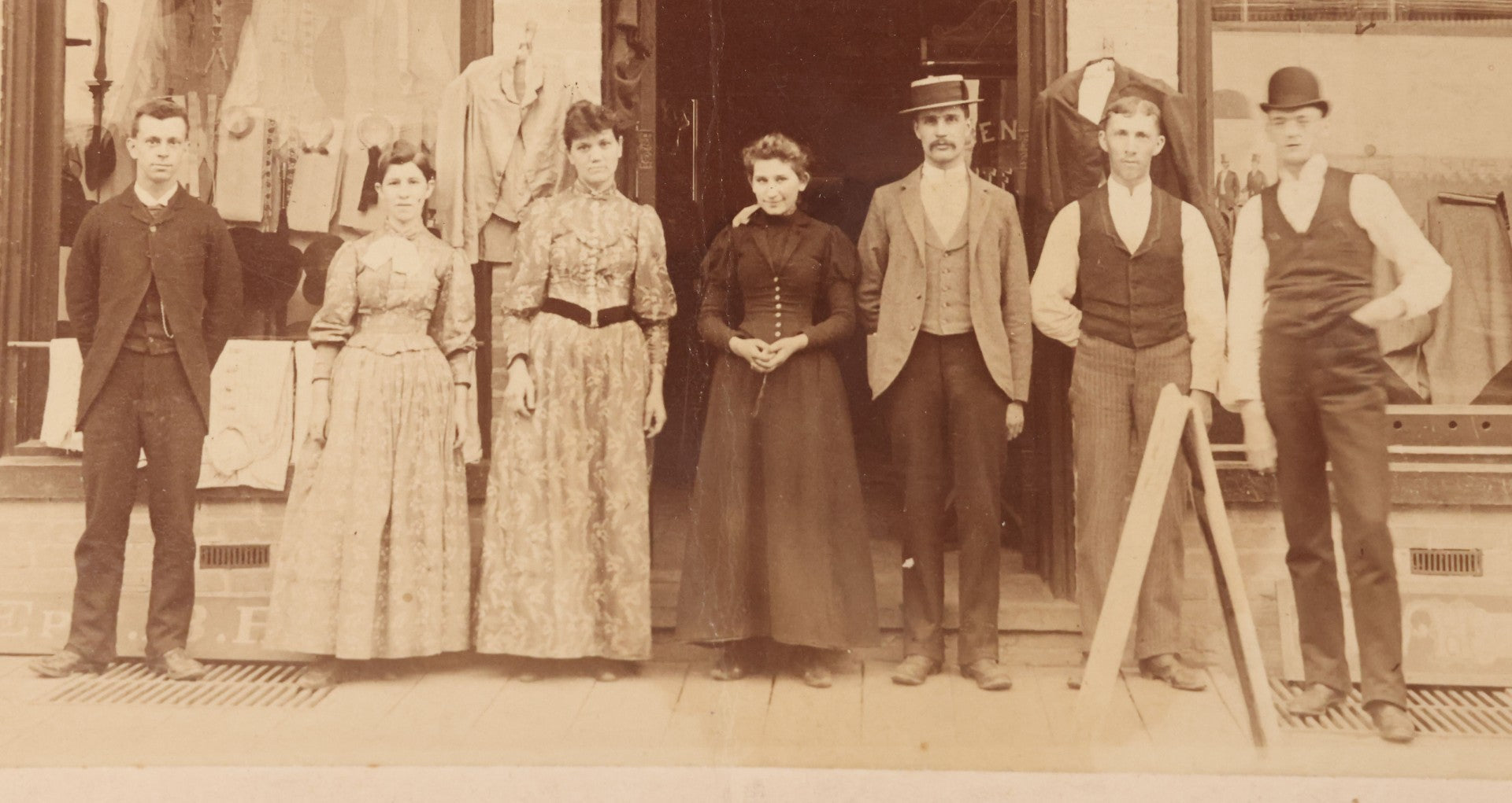 Lot 111 - Antique Boarded Occupational Photograph Of Workers And Dressmakers Posing Outside Their Shop, With Many Signs And Advertisements In Photo, Note Photo Has Large Crease Through Center On Verso