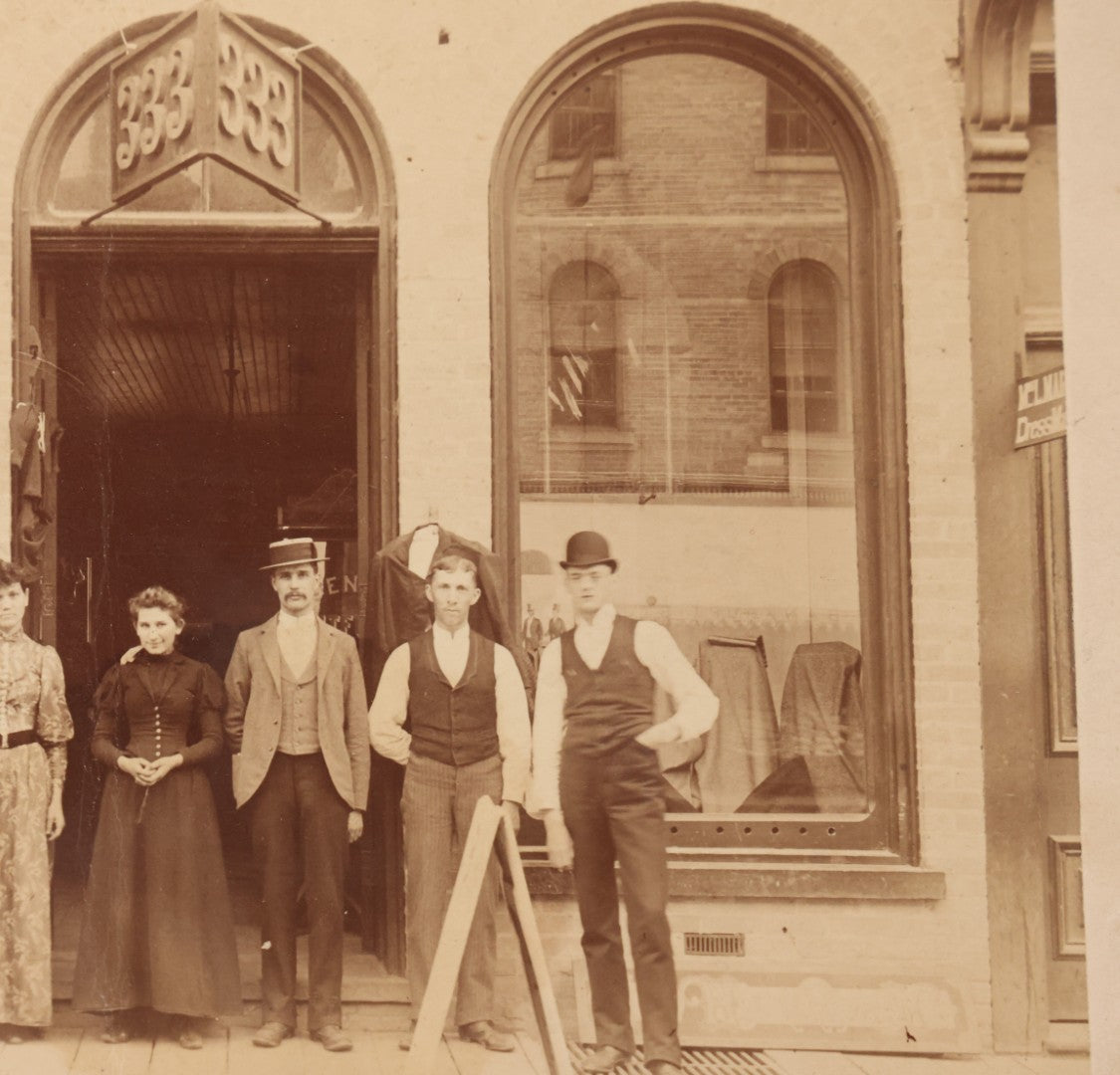 Lot 111 - Antique Boarded Occupational Photograph Of Workers And Dressmakers Posing Outside Their Shop, With Many Signs And Advertisements In Photo, Note Photo Has Large Crease Through Center On Verso
