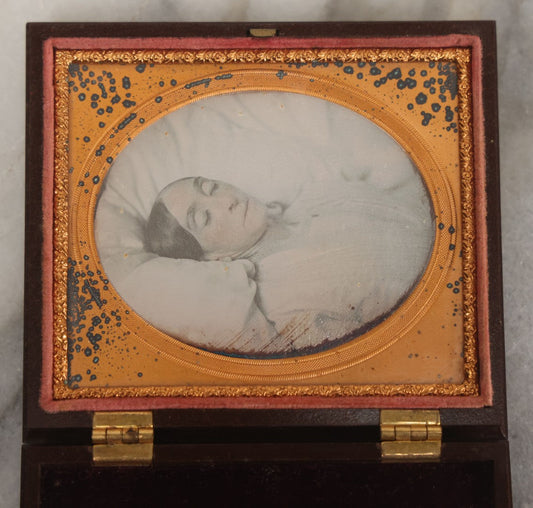 Lot 001 - Antique Victorian 1/6th Plate Color Tinted Daguerreotype Post Mortem Photograph Of A Deceased Woman At Rest On White Linens, In Original Thermoplastic "Genuine Union Case," Patented By S. Peck, 1854 And H. Halverson, 1855