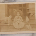 Lot 094 - Antique Boarded Photograph Of A Little Girl Posing On Porch With Her Toys: A Black Doll, Lamb Pull Toy, Dog Pull Toy, And Bunny Rocker,