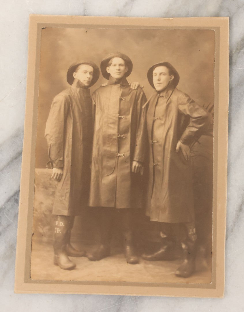 Lot 045 - Antique Trimmed Boarded Photograph Of Three Firefighters In Hats And Slickers Boots Marked J.F.D.