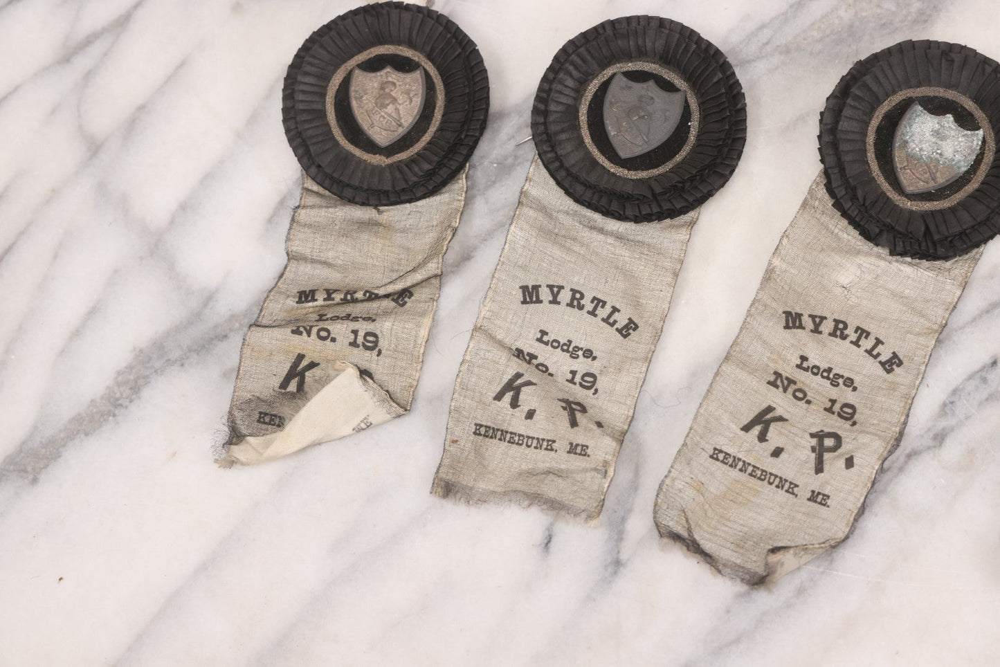 Lot 013 - Grouping Of 15+ Antique Knights Of Pythias Fraternal Badges And Ribbons With Black Coloring, White Ribbons With Black Veil Covering, Pressed Metal Insignia, Myrtle Lodge No. 19, K.P., Kennebunk, Maine