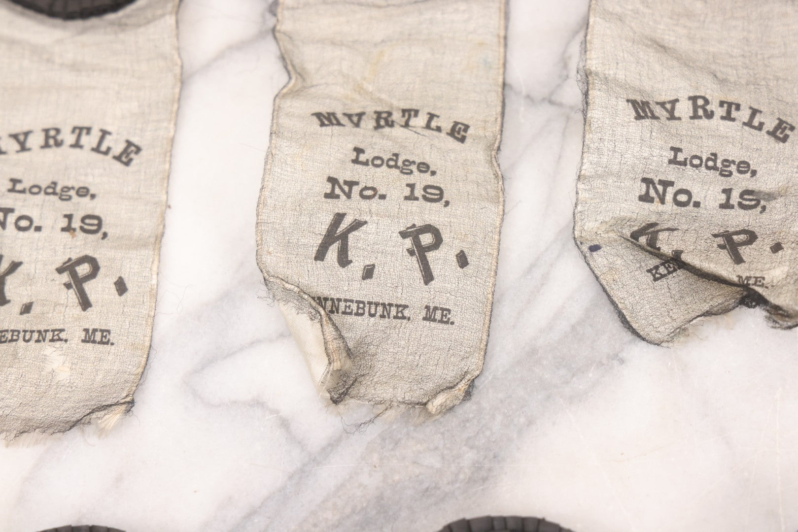 Lot 013 - Grouping Of 15+ Antique Knights Of Pythias Fraternal Badges And Ribbons With Black Coloring, White Ribbons With Black Veil Covering, Pressed Metal Insignia, Myrtle Lodge No. 19, K.P., Kennebunk, Maine