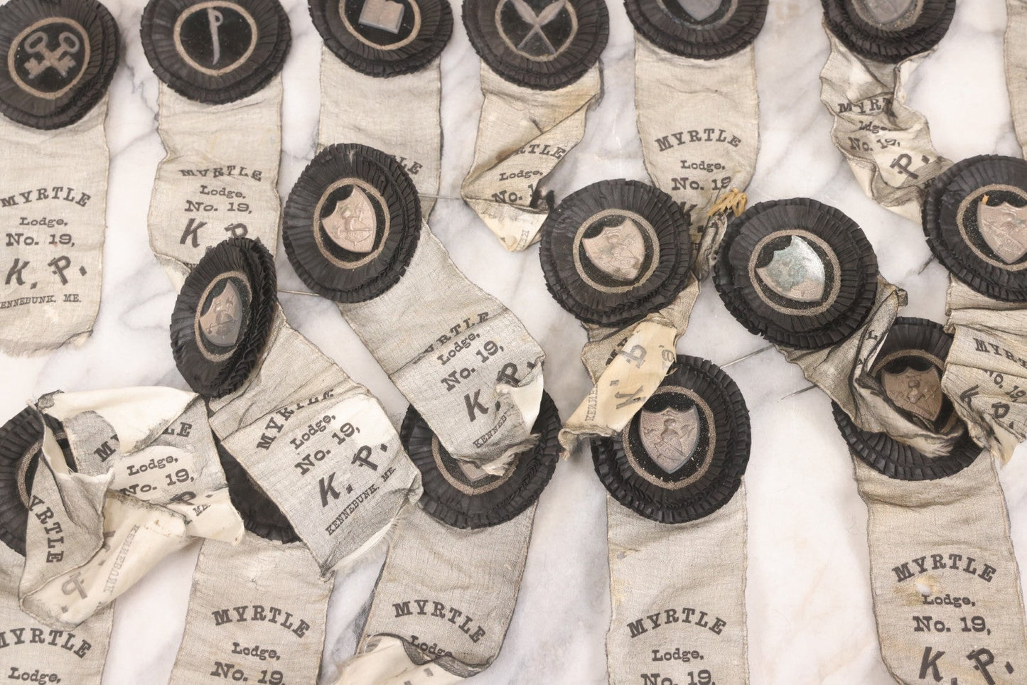 Lot 013 - Grouping Of 15+ Antique Knights Of Pythias Fraternal Badges And Ribbons With Black Coloring, White Ribbons With Black Veil Covering, Pressed Metal Insignia, Myrtle Lodge No. 19, K.P., Kennebunk, Maine