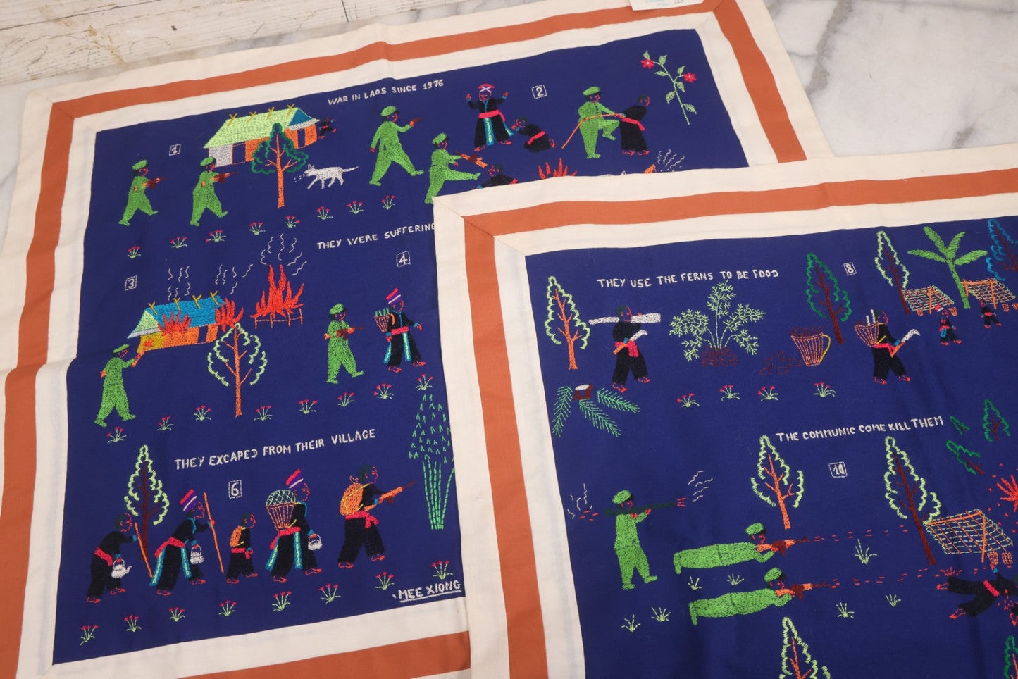 Lot 017 - Pair Of Vintage Folk Art Embroidered Hmong Story Cloths (Paj Ntaub) Illustrating "The War In Laos Since 1976" Across 13 Scenes, Artist Signed Mee Xiong, With Gallery Label From Cama Crafts, Made In Thailand, Circa 1990s