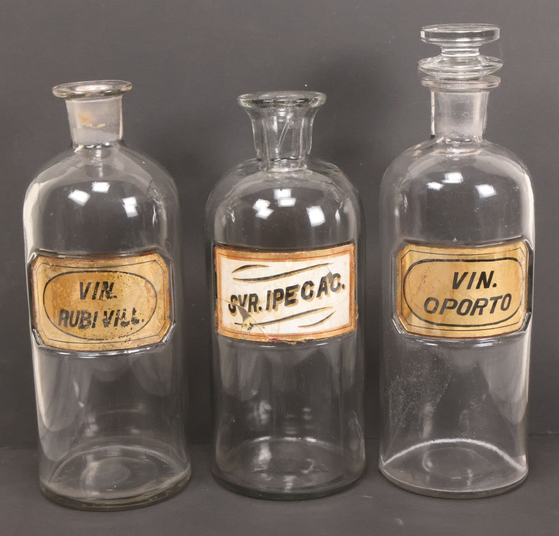 Lot 057 - Grouping Of Three Antique Glass Apothecary Bottles With Reverse Painted Glass Labels Including Syrup Of Ipecac (Syr. Ipecac.), Blackberry Wine (Vin. Rubi Vill.), And Port Wine (Vin. Oporto)