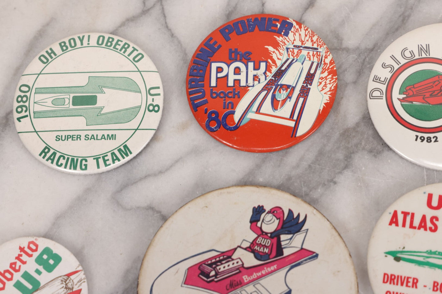 Lot 094 - Vintage Grouping Of 12 Buttons, Including Signed Jerry Hopp Button, "Super Salami" Racing Buttons, Vote For Kermit Button, Others