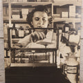 Lot 144 - Vintage Large Cardboard Mount Black And White Photograph Print Of Woman Pharmacist Measuring Drugs From Antique Glass Label Apothecary Jar, Many Drugs On Shelves In Background, 13-1/4" x 16-1/2"