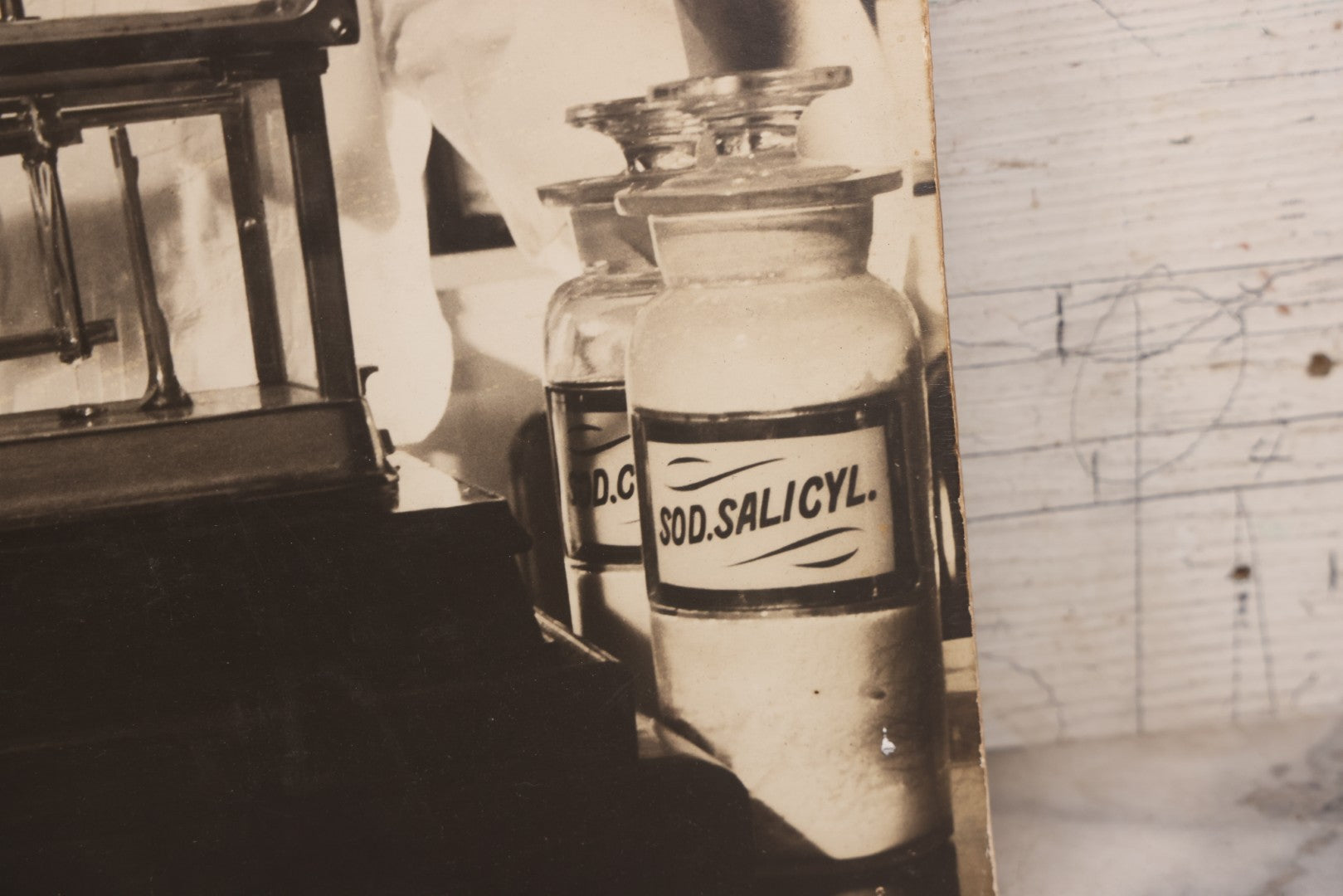 Lot 144 - Vintage Large Cardboard Mount Black And White Photograph Print Of Woman Pharmacist Measuring Drugs From Antique Glass Label Apothecary Jar, Many Drugs On Shelves In Background, 13-1/4" x 16-1/2"