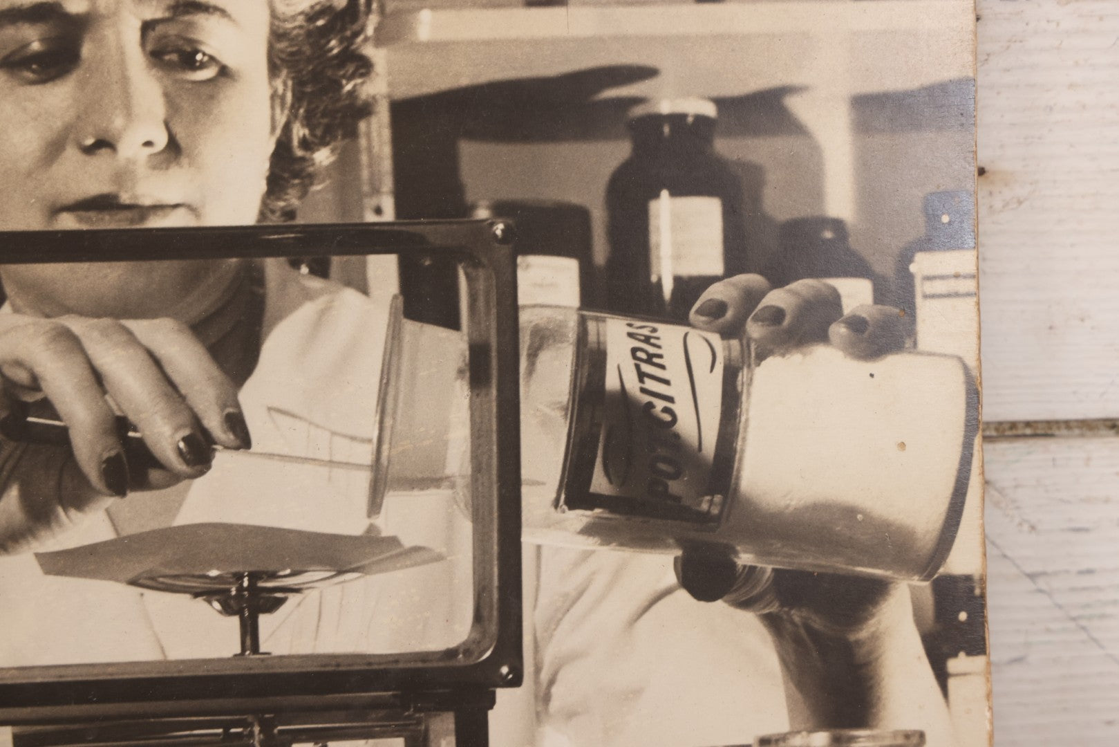 Lot 144 - Vintage Large Cardboard Mount Black And White Photograph Print Of Woman Pharmacist Measuring Drugs From Antique Glass Label Apothecary Jar, Many Drugs On Shelves In Background, 13-1/4" x 16-1/2"