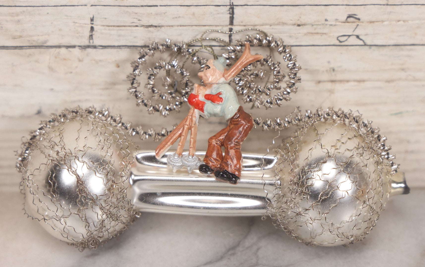 Lot 155 - Vintage Tinsel And Tin And Wire Christmas Ornament Featuring Plastic Skier Holding Skis And Ski Poles With Red Gloves, Barbell Shape, 4-3/4" Length