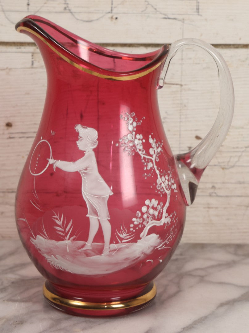 Lot 042 -  Antique Mary Gregory Style Cranberry Glass Pitcher Hand Painted Enamel Decoration Of Boy Playing Hoop And Gold Trim