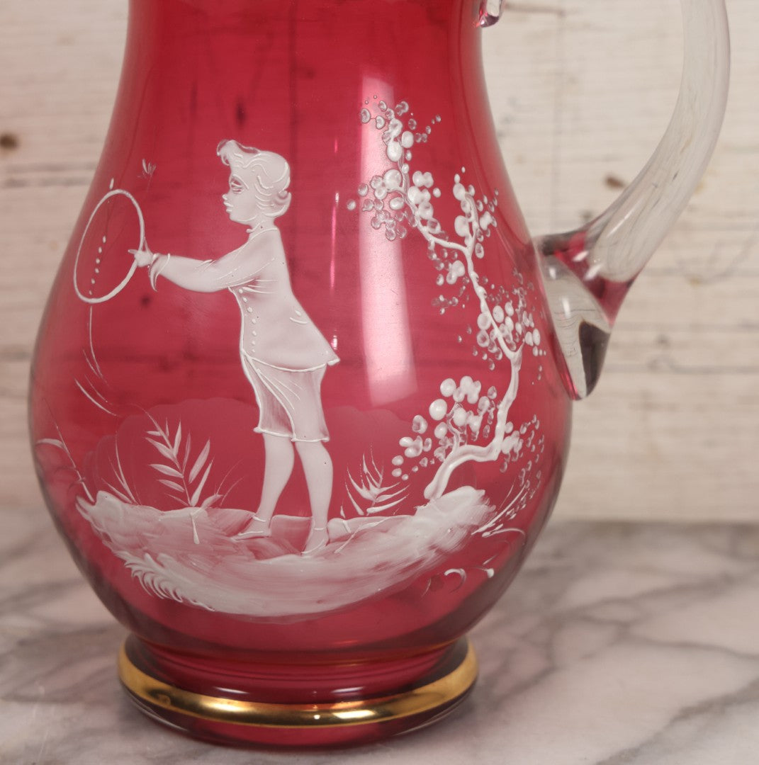 Lot 042 -  Antique Mary Gregory Style Cranberry Glass Pitcher Hand Painted Enamel Decoration Of Boy Playing Hoop And Gold Trim