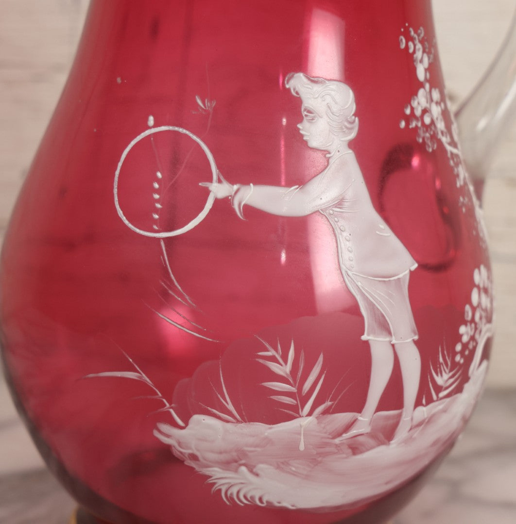 Lot 042 -  Antique Mary Gregory Style Cranberry Glass Pitcher Hand Painted Enamel Decoration Of Boy Playing Hoop And Gold Trim