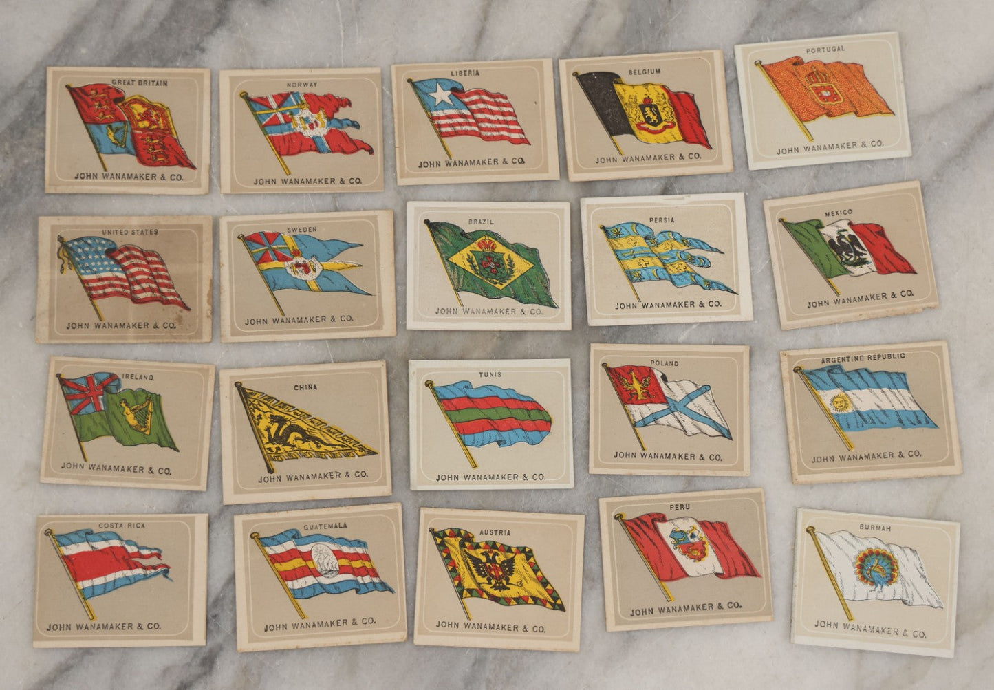Lot 254 - Grouping Of Twenty Antique Lithgraphed Trade Card Advertisements Showing The Flags Of The World, Advertising John Wanamaker & Co., Clothing, Philadelphia, Pennsylvania 