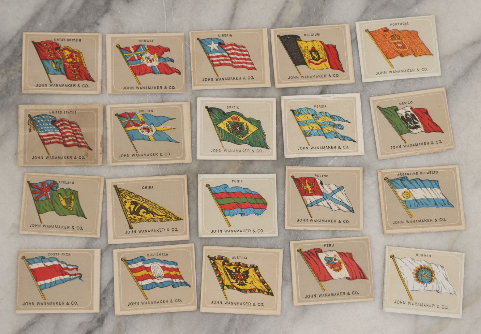 Lot 254 - Grouping Of Twenty Antique Lithgraphed Trade Card Advertisements Showing The Flags Of The World, Advertising John Wanamaker & Co., Clothing, Philadelphia, Pennsylvania 