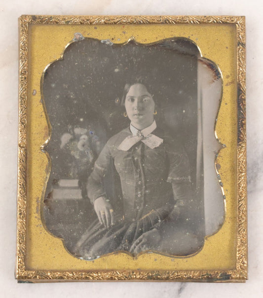 Lot 030 - Antique Uncased 1/6th Plate Daguerreotype Photograph Of A Young Woman Posing With A Table, Flowers, And Books, With Brass Mat And Preserver