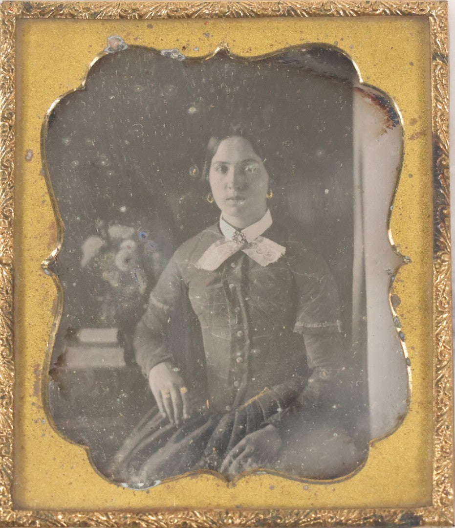 Lot 030 - Antique Uncased 1/6th Plate Daguerreotype Photograph Of A Young Woman Posing With A Table, Flowers, And Books, With Brass Mat And Preserver