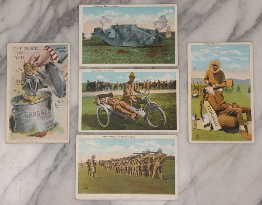 Lot 082 - Grouping Of Five Antique World War One Era Postcards Documenting The War Including Comic Illustration, Uncle Sam Placing Kaiser In Garbage, Soldier Shaving, Tank In Action, Motorcycle Ambulance, And Rifle Practice