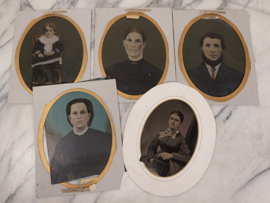 Lot 087 - Grouping Of Five Full Plate Portrait Tintypes Of Men, Women And Children, With Oval Cut Paper Frames With Gold Painted Border, Including Four Hand Colored Photos