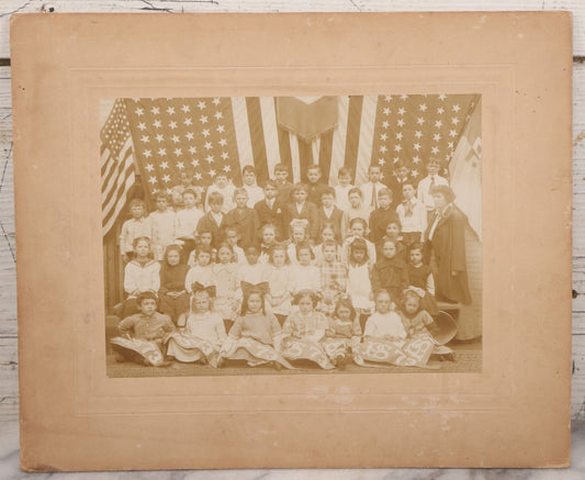 Lot 069 - Antique Boarded Photograph Of An Integrated Elementary School Class, Posing With Large 48 Star American Flag Bunting And Patriotic Decor, Pennants From P.S. 73, Teacher In Photo, Circa 1895